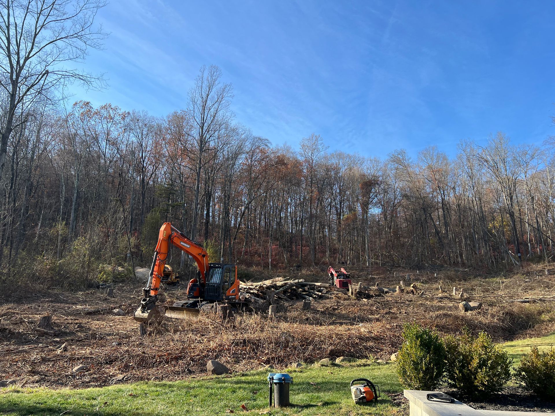 A large excavator is working in a field with trees in the background.