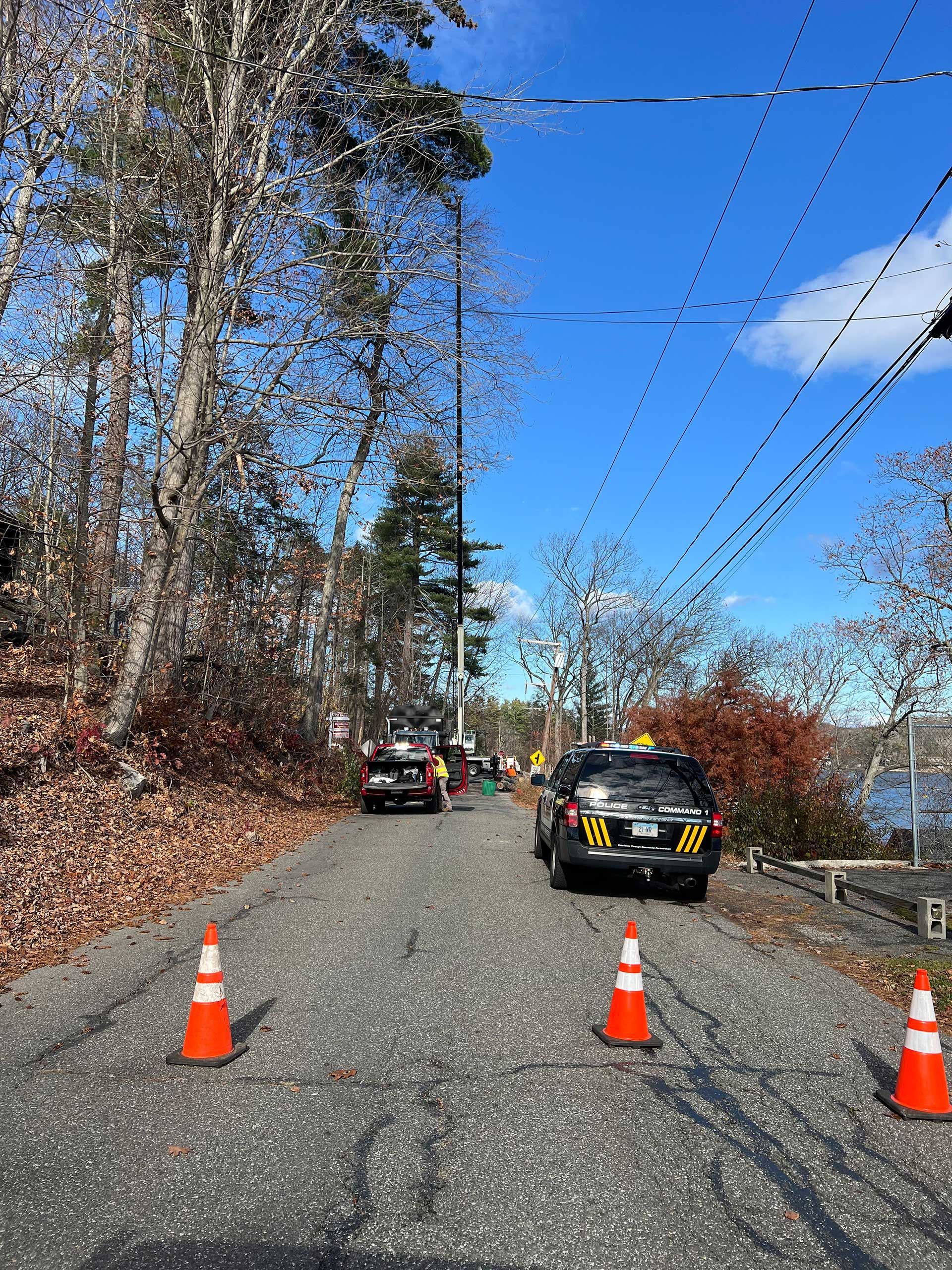 narrow road blocked by orange cones, two utility vehicles with flashing lights parked ahead