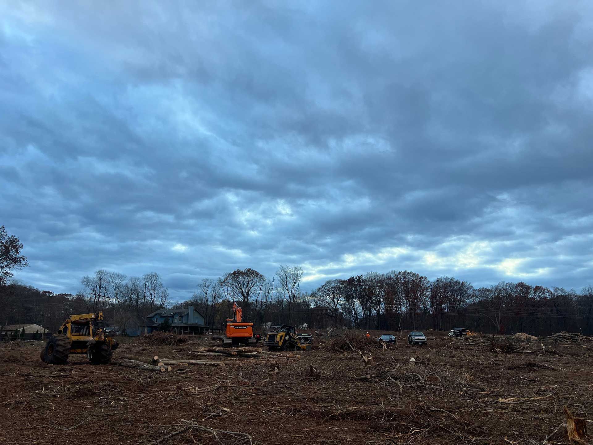 clearing for construction: brown field, heavy machinery, bare trees under a cloudy sky