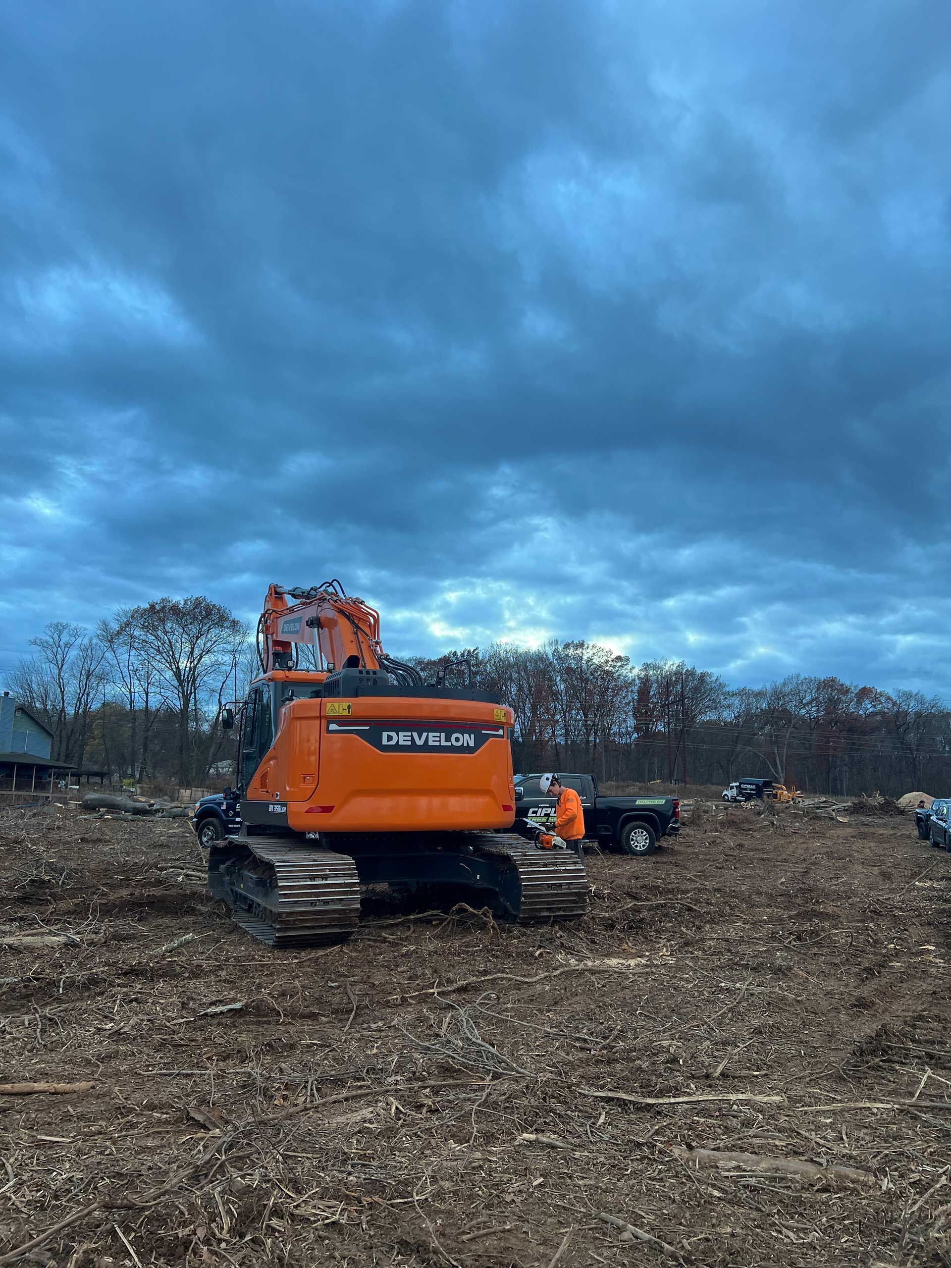 orange excavator on a wood-chipped surface under a cloudy sky