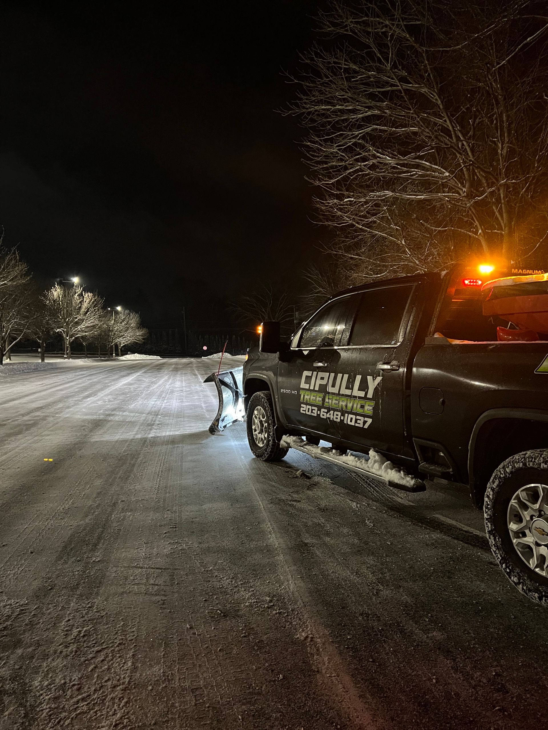A truck is driving down a snowy road at night.