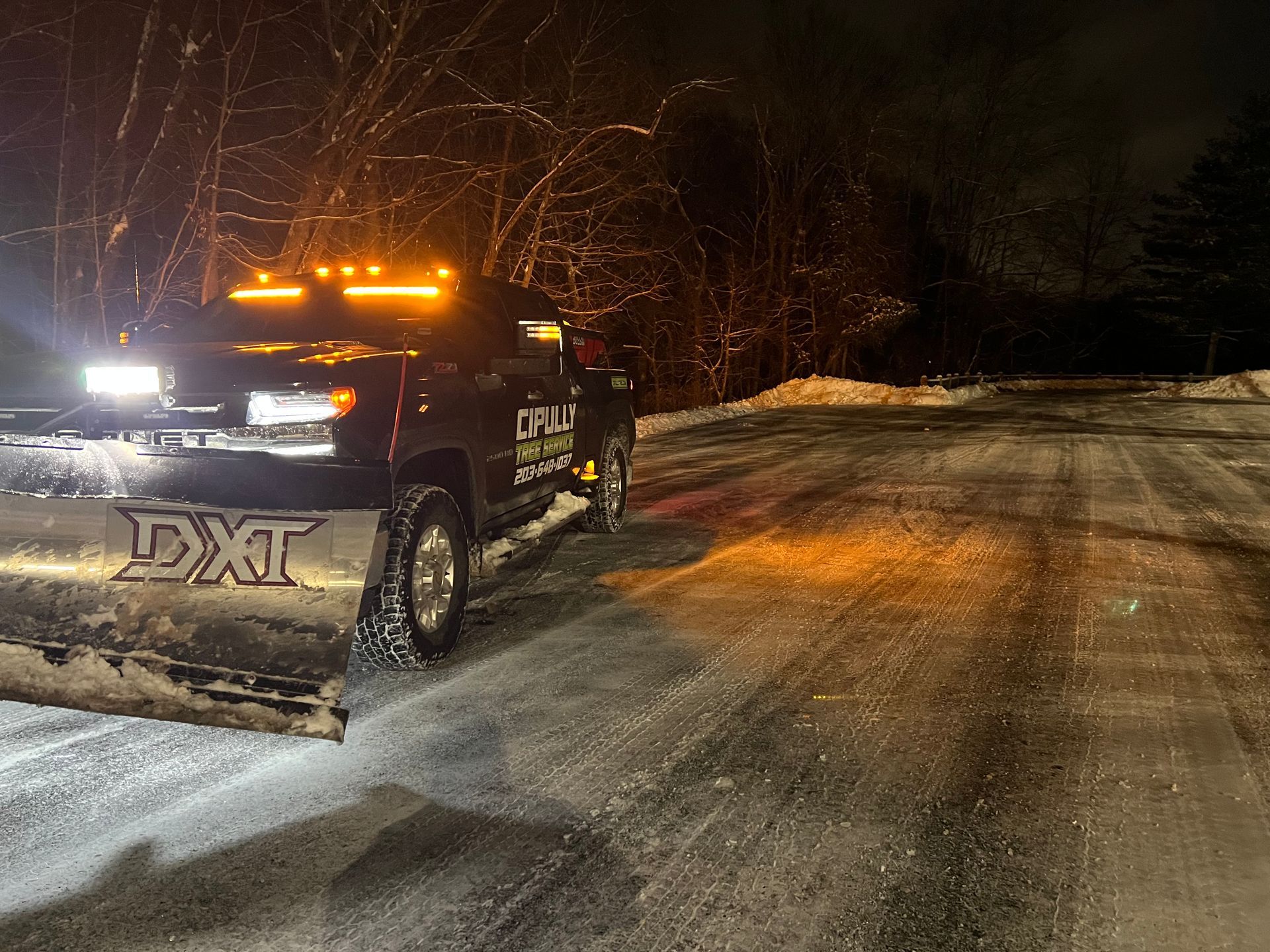 A snow plow is driving down a snowy road at night.
