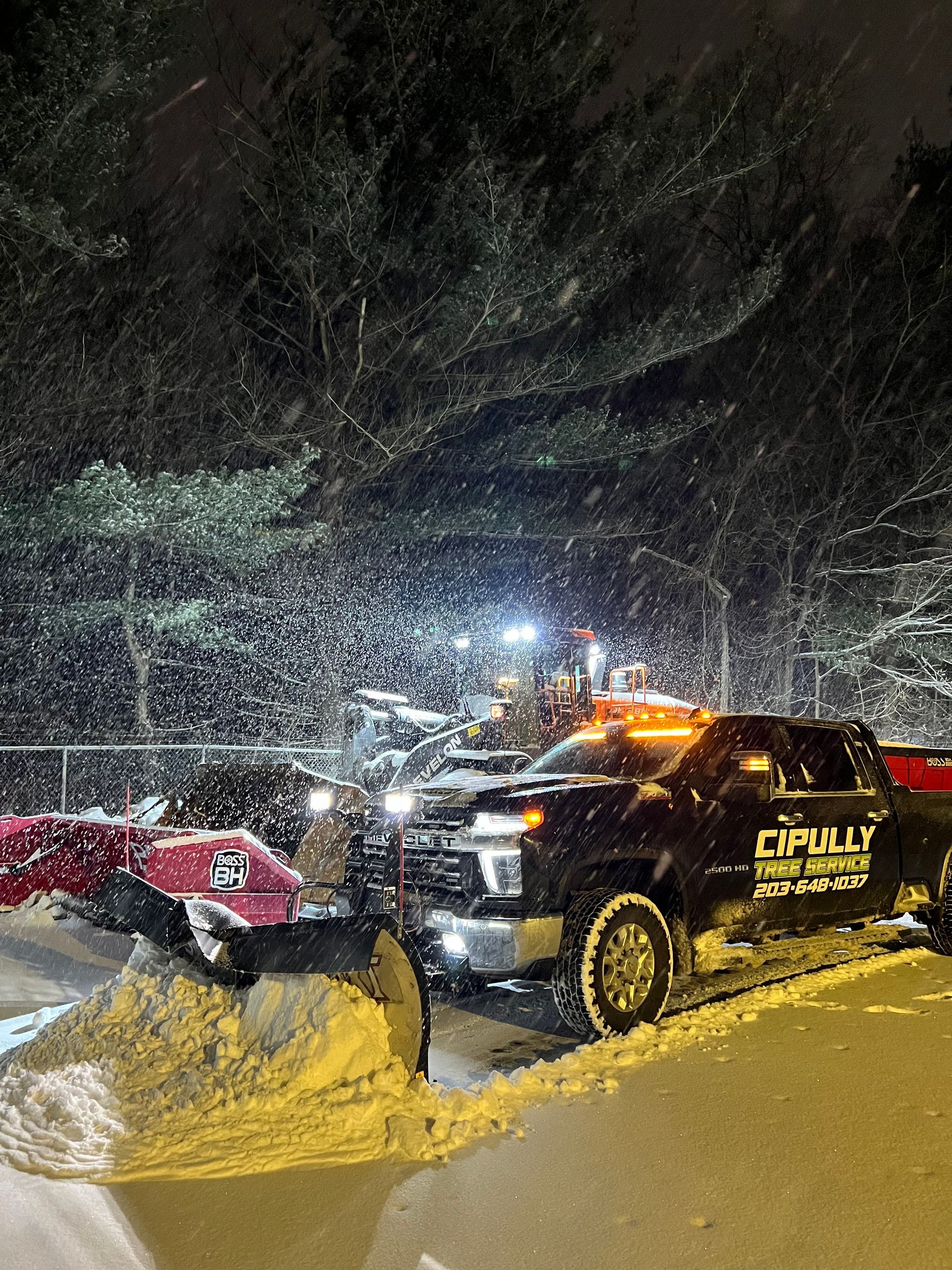 A truck is plowing snow in a parking lot at night.