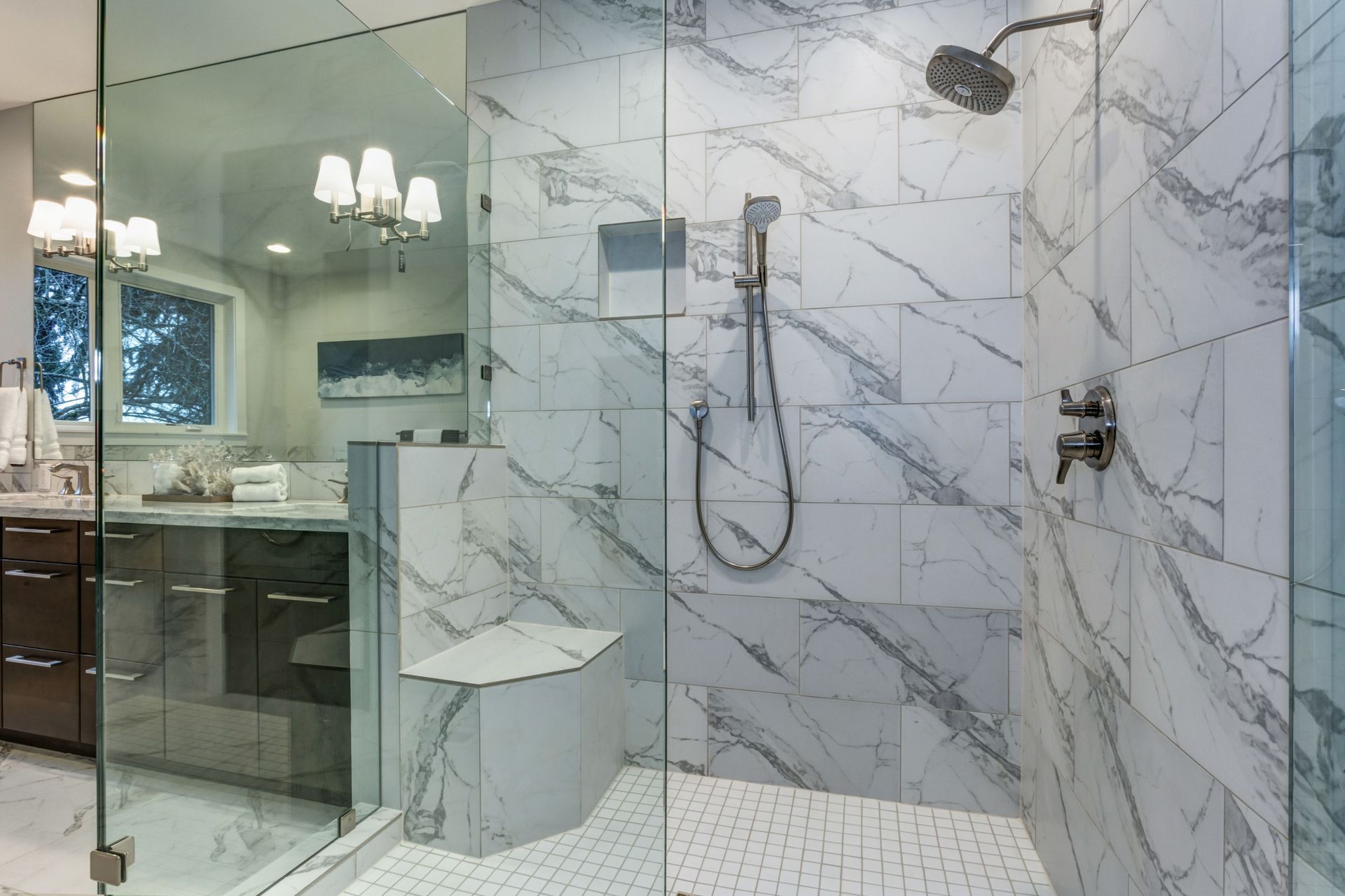 Modern marble-tiled bathroom with glass shower, bench, and vanity beyond the glass door