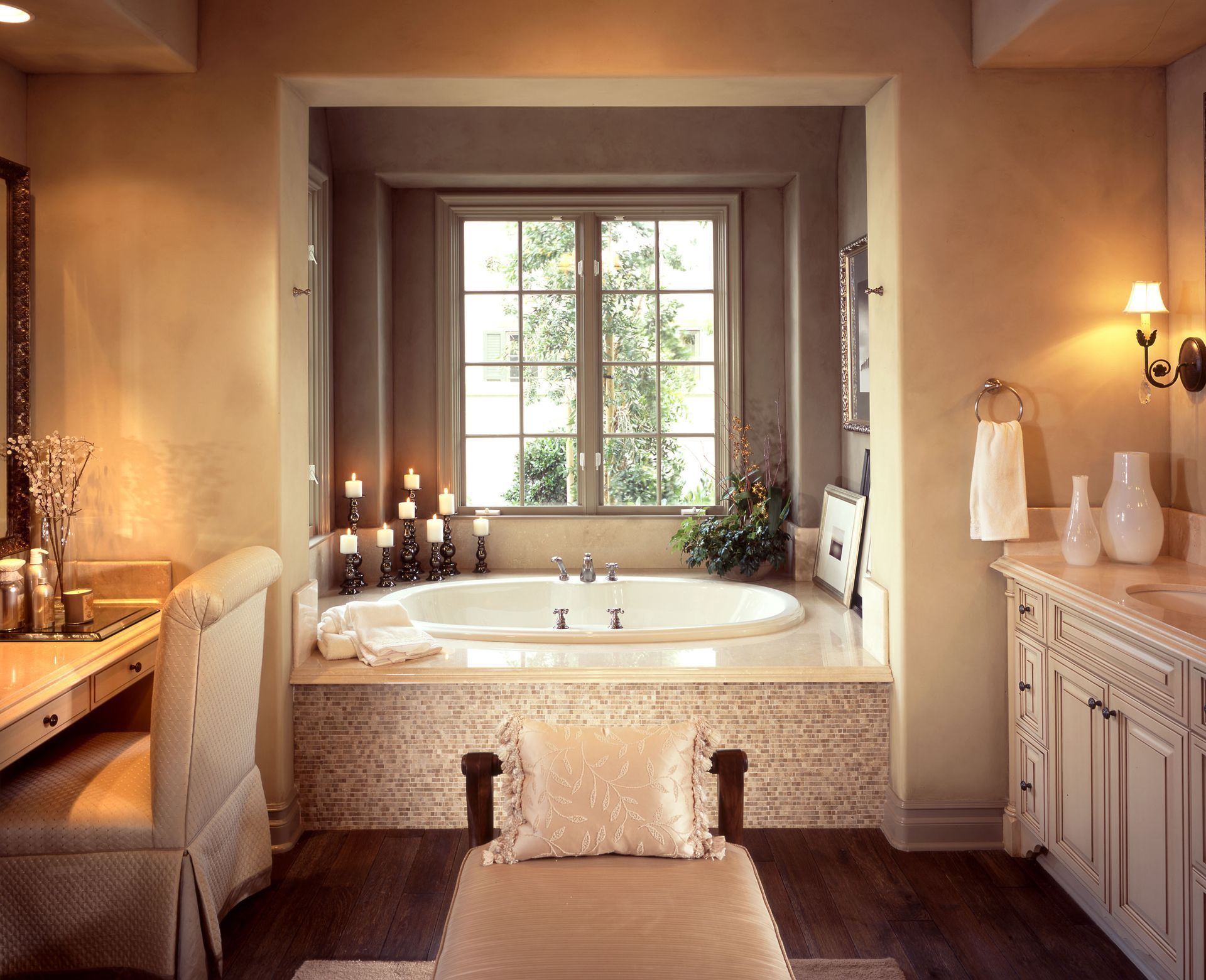 Elegant bathroom with a freestanding tub by a window, warm beige tones, and soft candles lighting the space