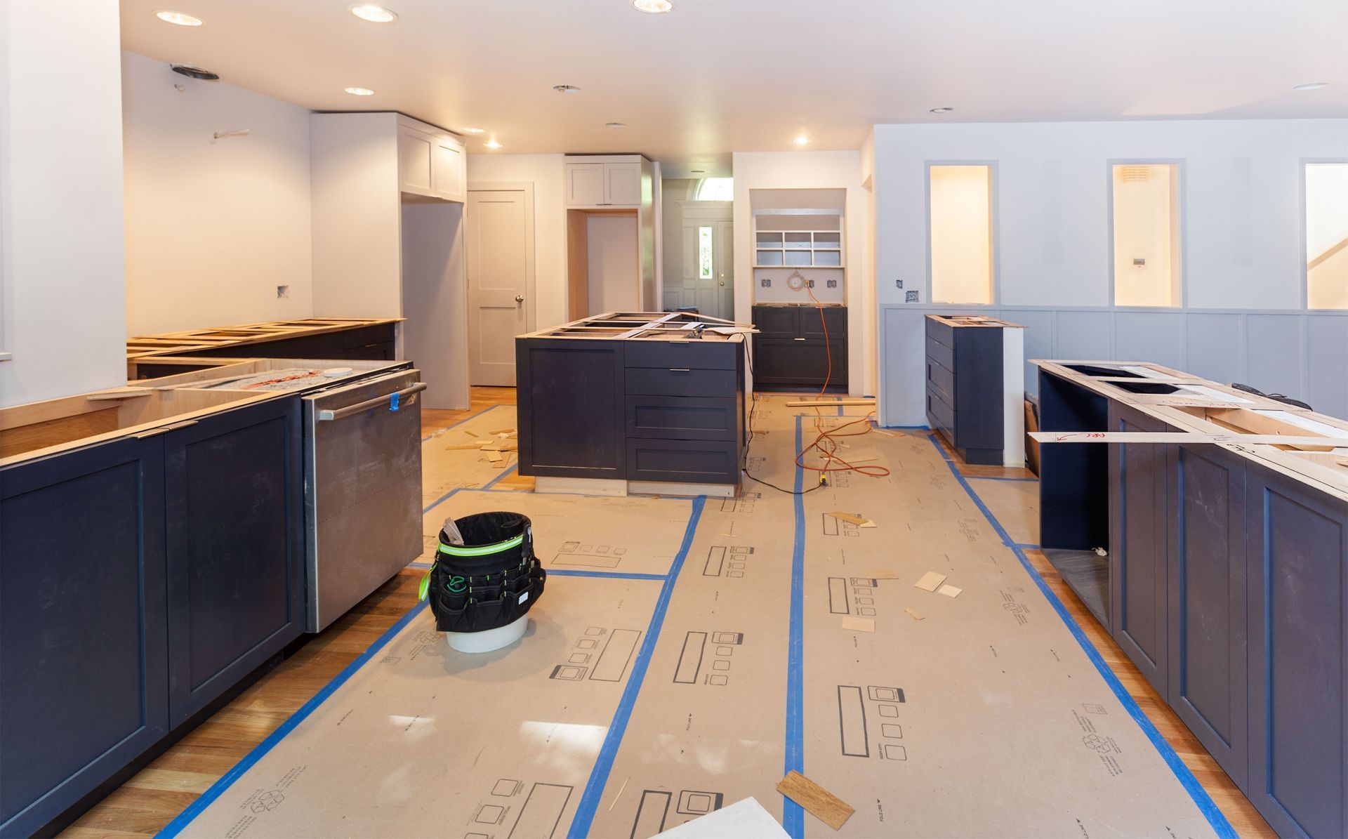 Kitchen under renovation with blue cabinets, covered floors, and work materials