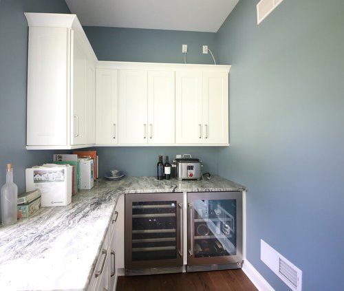 Bright kitchen corner with white cabinets, gray walls, granite counter, and a stainless mini fridge and wine cooler.