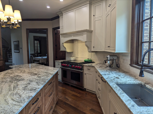 Bright kitchen with white cabinets, granite counters, herringbone wood floor, stove, and large island.