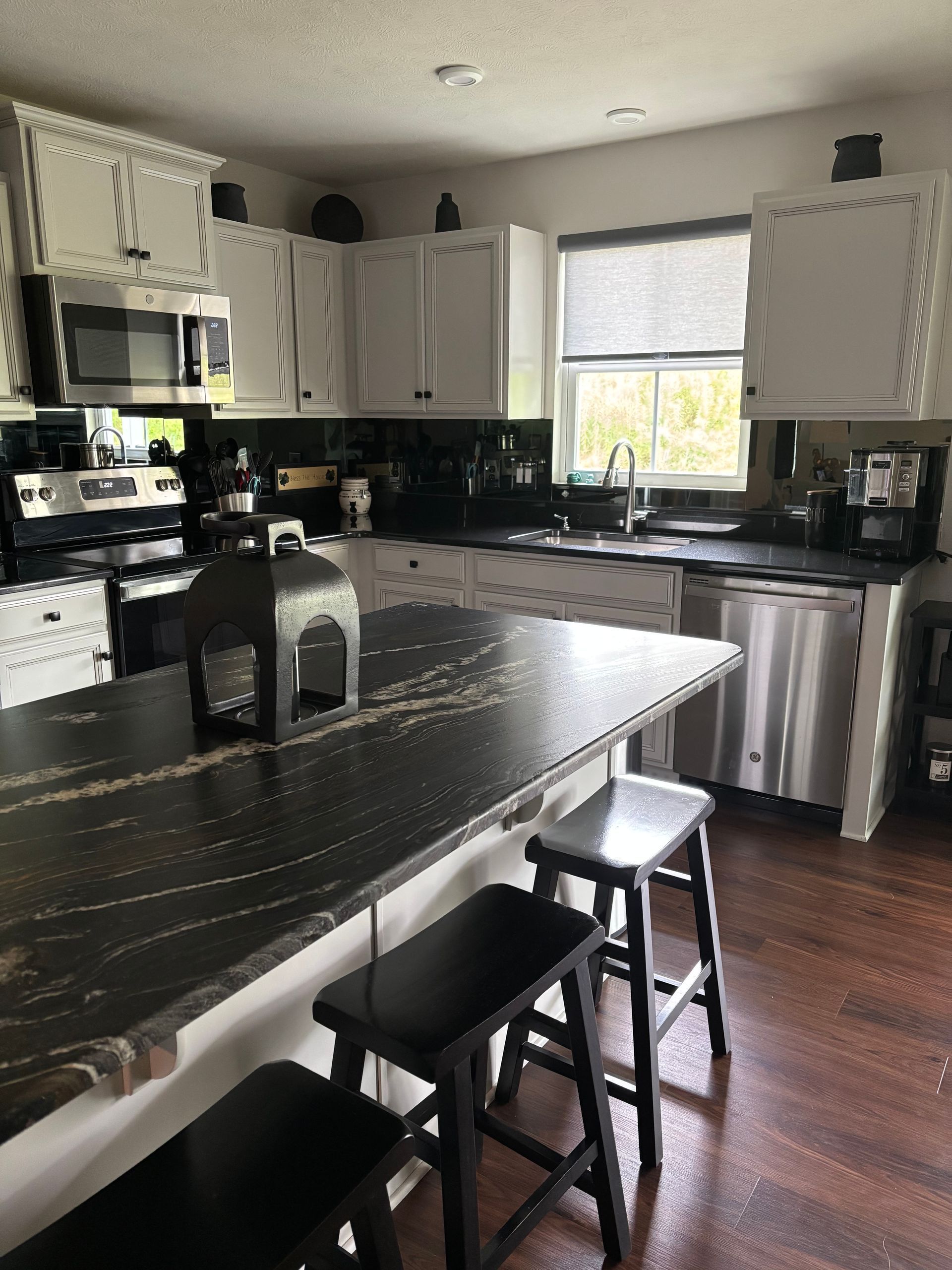Modern kitchen with black island, white cabinets, and two stools by a window