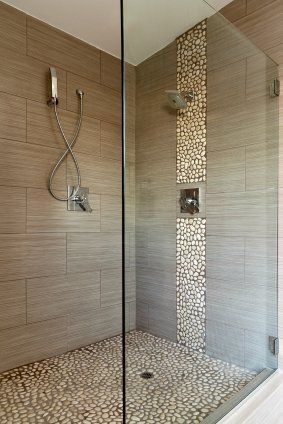 Modern tiled walk-in shower with glass door, rain showerhead, and pebble stone accent wall and floor