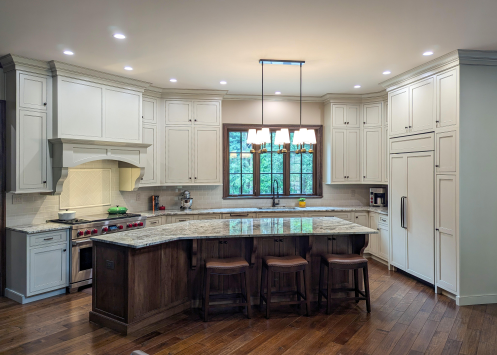Bright white kitchen with granite island, dark wood floor, and a window above the sink.