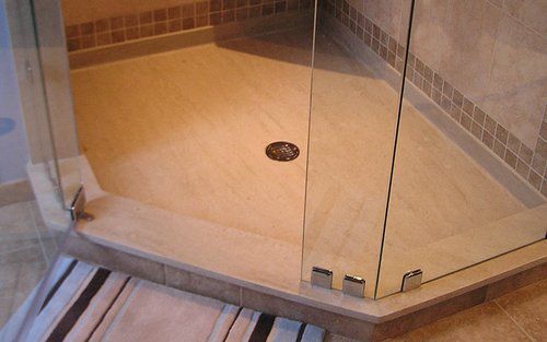 Corner glass shower stall with beige tiled floor and chrome drain