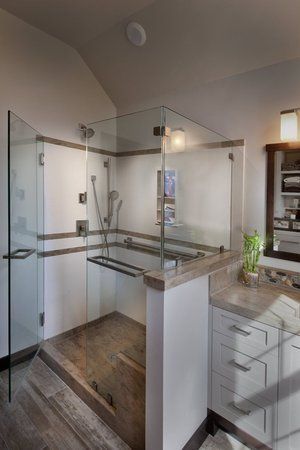 Modern bathroom shower with glass doors, gray tile floor, and a vanity on the right