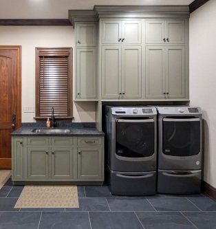 Laundry room with green cabinets, black countertop, sink, and two front-loading washers on dark tile floor