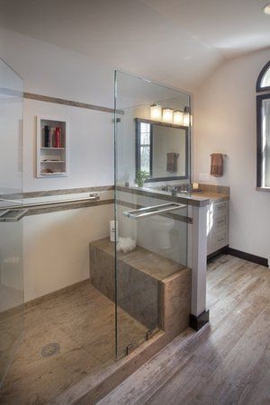 Modern bathroom with glass shower enclosure, stone bench, and vanity sink under a mirror.