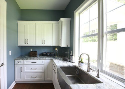 Bright kitchen with white cabinets, blue walls, marble counters, and a large window over the sink.