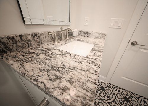 White bathroom vanity with speckled granite countertop and built-in sink beside a closed door