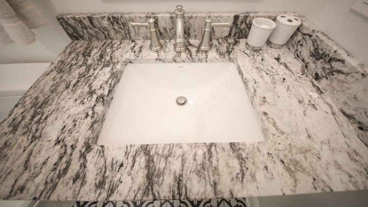 Marble bathroom vanity with white sink, chrome faucet, and two white cups on the right side.