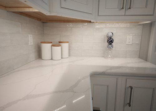 White kitchen countertop with light gray tile backsplash and canisters under cabinets