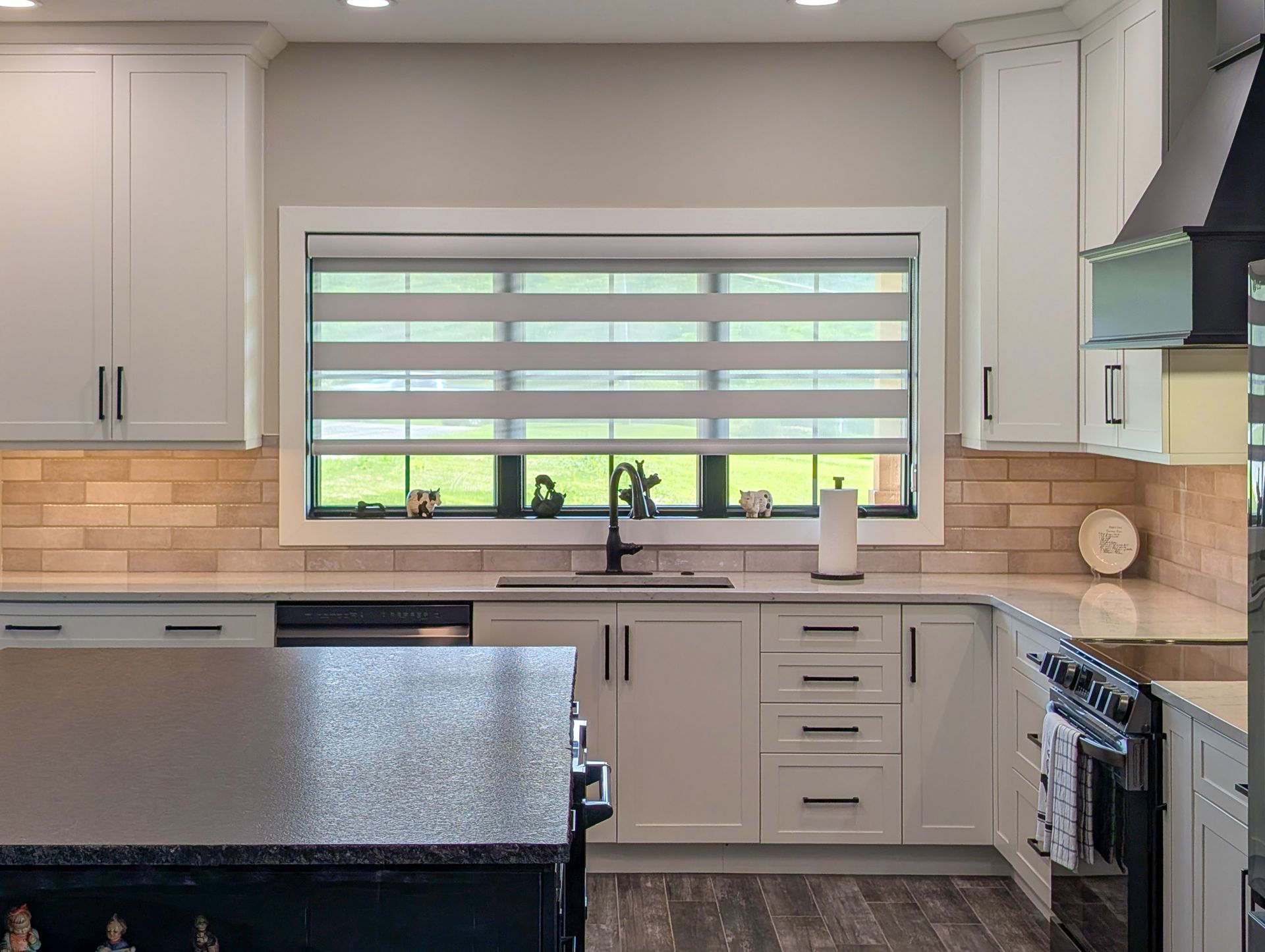 Modern kitchen with gray cabinets, black countertops, window over sink, and stainless appliances