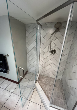 Modern walk-in shower with glass panel, herringbone tile wall, and chrome shower controls
