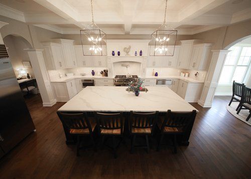 Bright white kitchen with a large island, dark bar stools, pendant lights, and a windowed dining nook