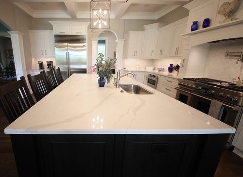 Modern white kitchen with large island, dark lower cabinets, and stainless steel appliances