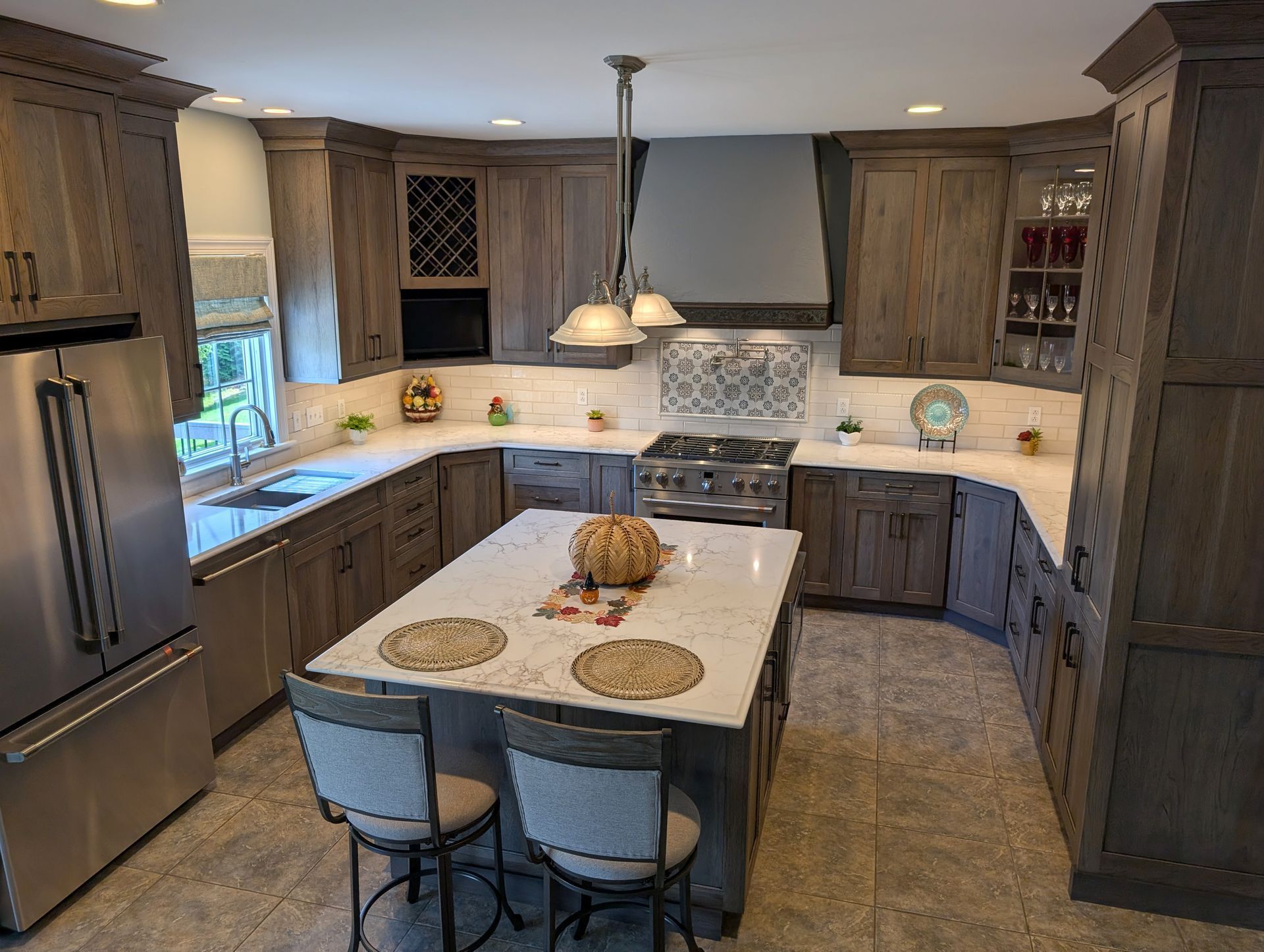 Modern kitchen with gray cabinets, stainless fridge, island, and pendant light over tiled floor