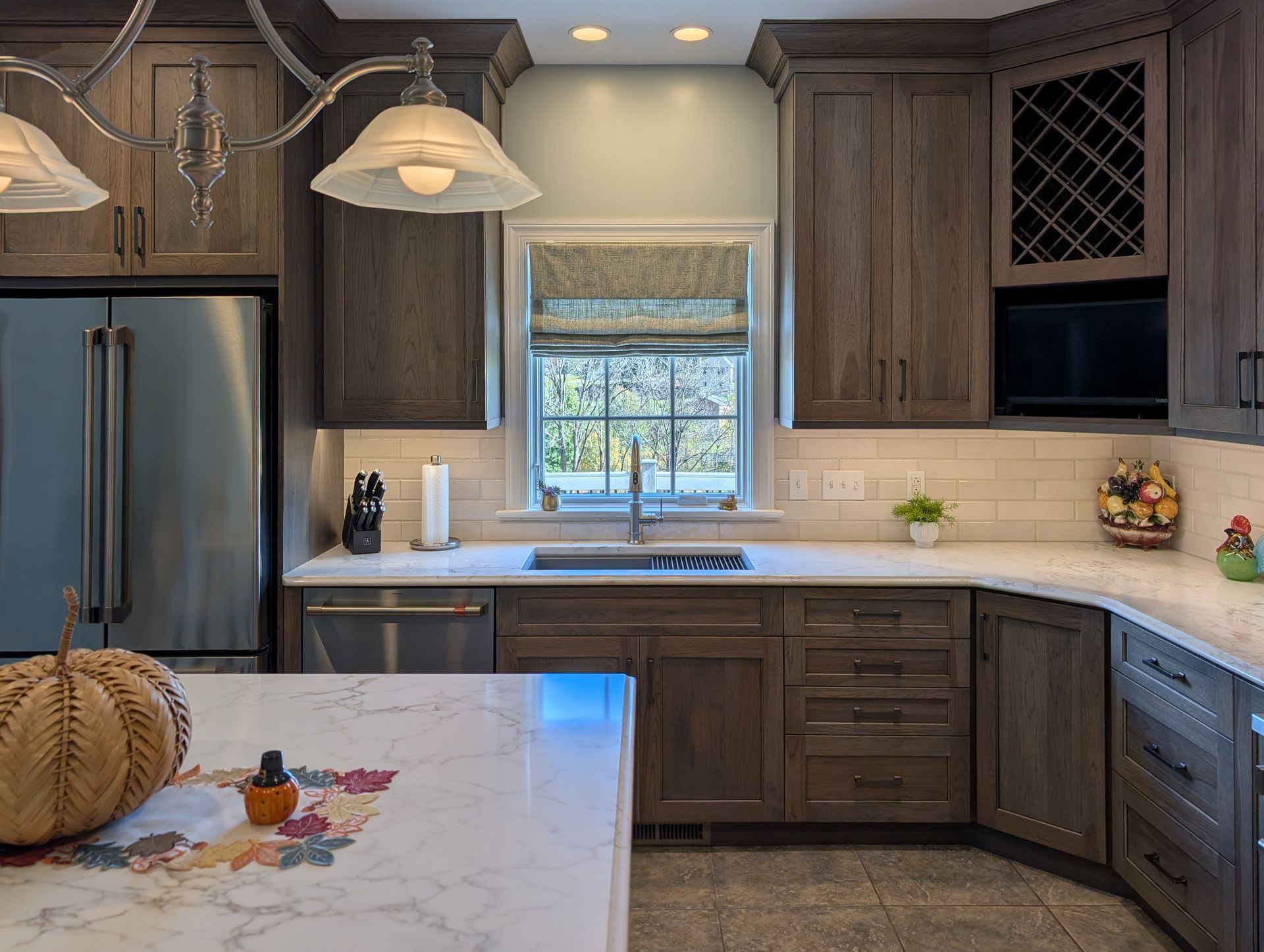 Modern kitchen with dark wood cabinets, stainless fridge, white countertops, and a window above the sink