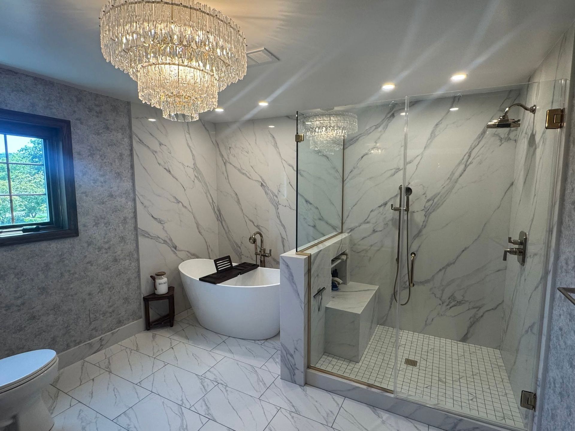 Elegant marble bathroom with chandelier, freestanding tub, vanity, and glass shower enclosure
