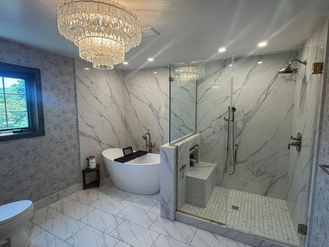 Luxurious marble bathroom with chandelier, freestanding tub, glass shower, and white tiled floor