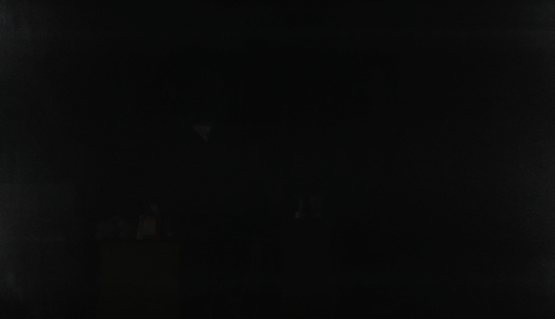 Mostly black, very dark scene with faint, barely visible shapes and lights in the distance.