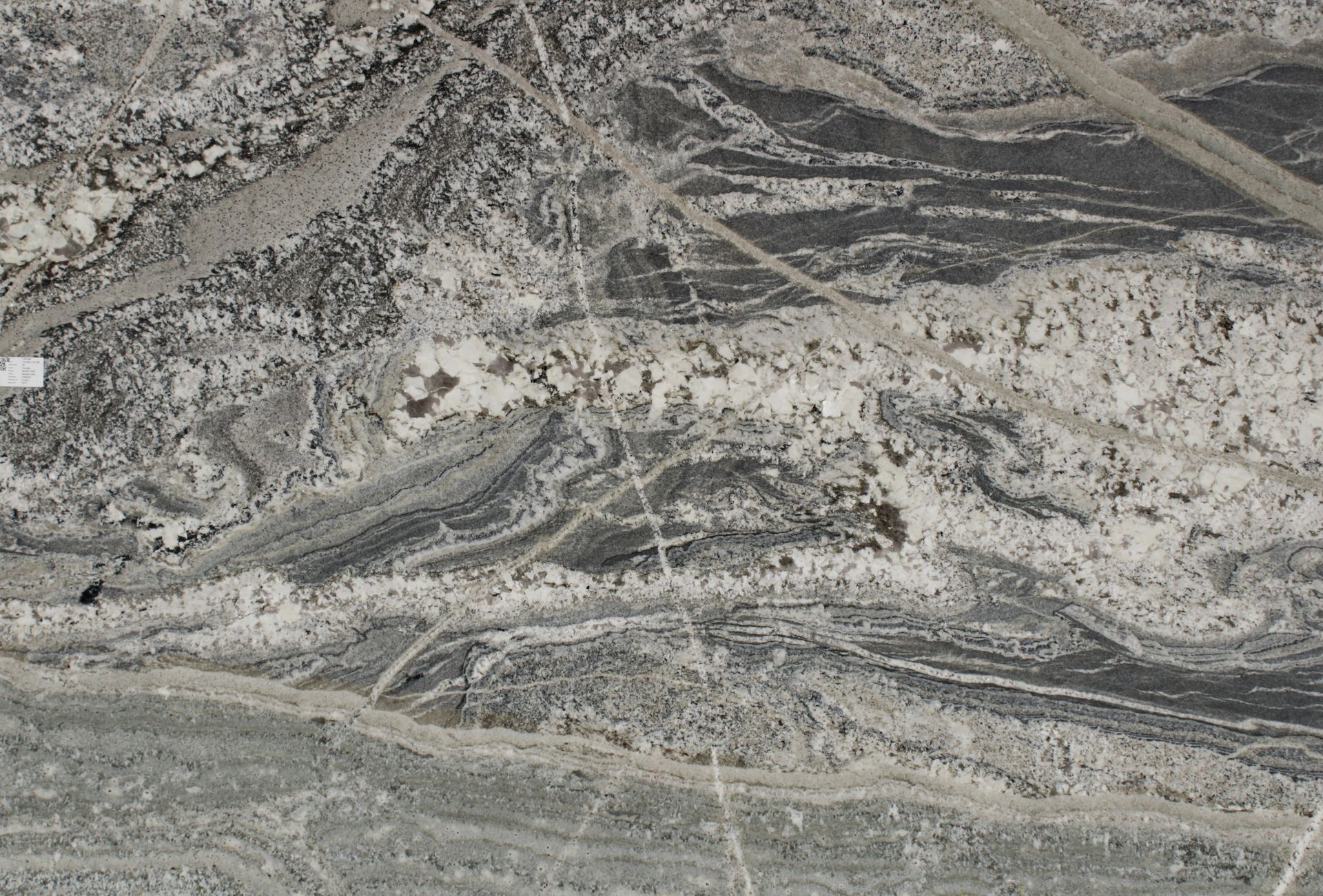 Aerial view of a gray, rocky landscape with winding layered patterns and scattered light-colored areas