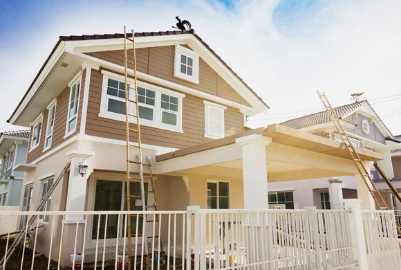 Two-story house under construction with ladders and scaffolding beside a white porch railing