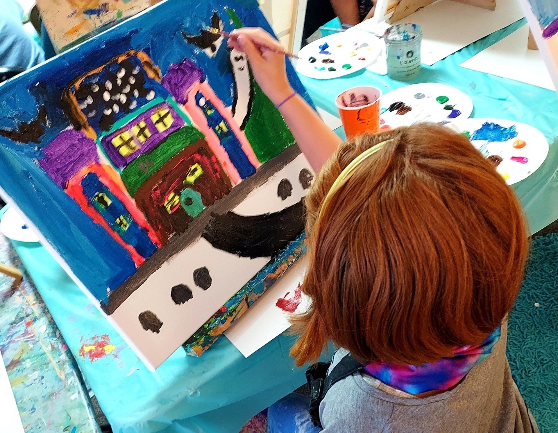 A little girl is painting a picture of a haunted house
