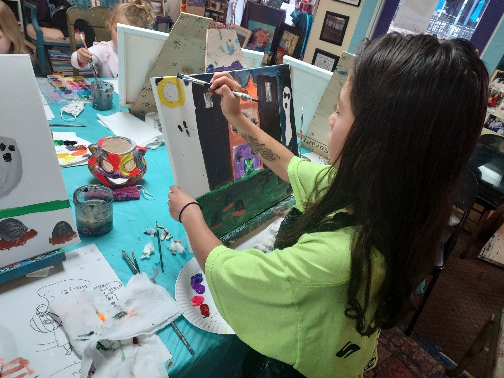 A young girl is sitting at a table painting a picture of a ghost.