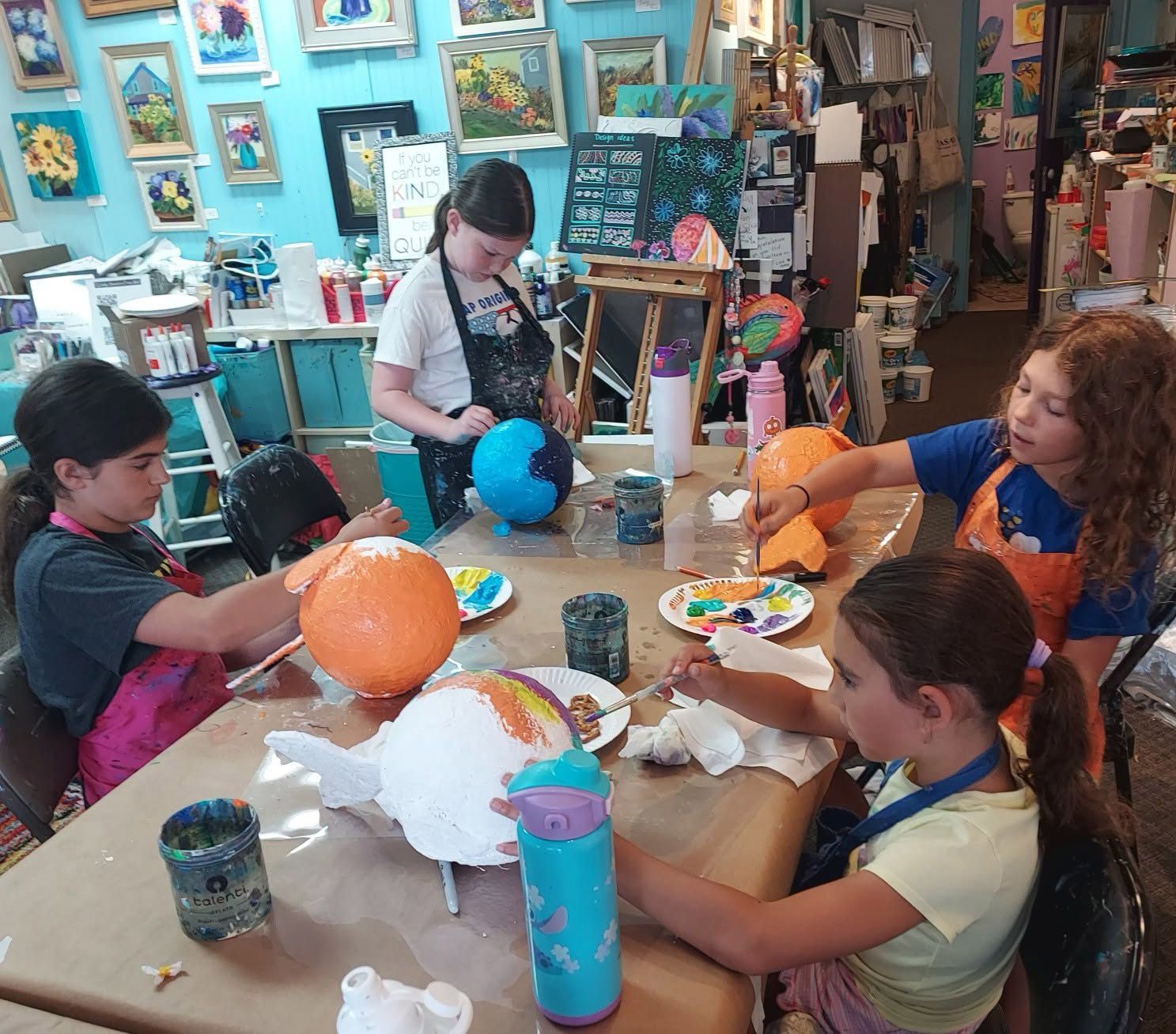 Children painting balloons at a craft table in a colorful classroom