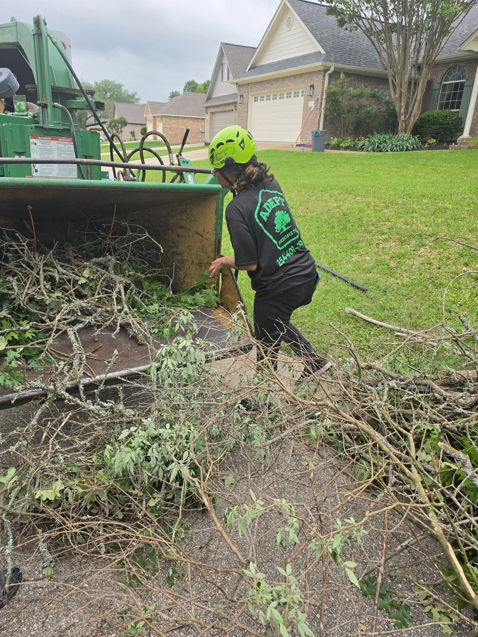 Worker in neon helmet clearing brush beside a green tractor in a suburban yard