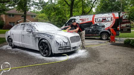 A man is washing a car with foam in a driveway.