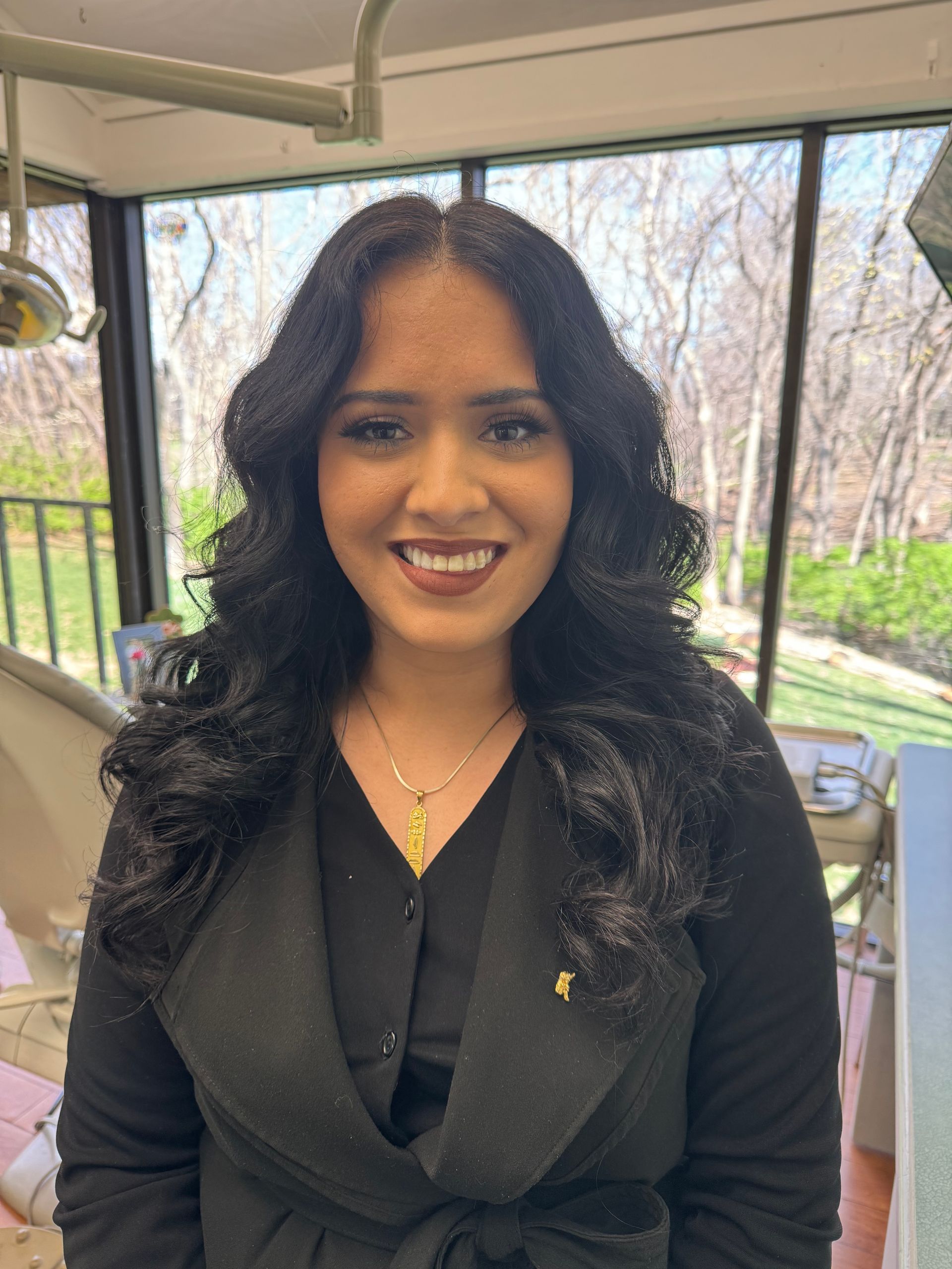 A woman with long black hair is smiling in a dental office.