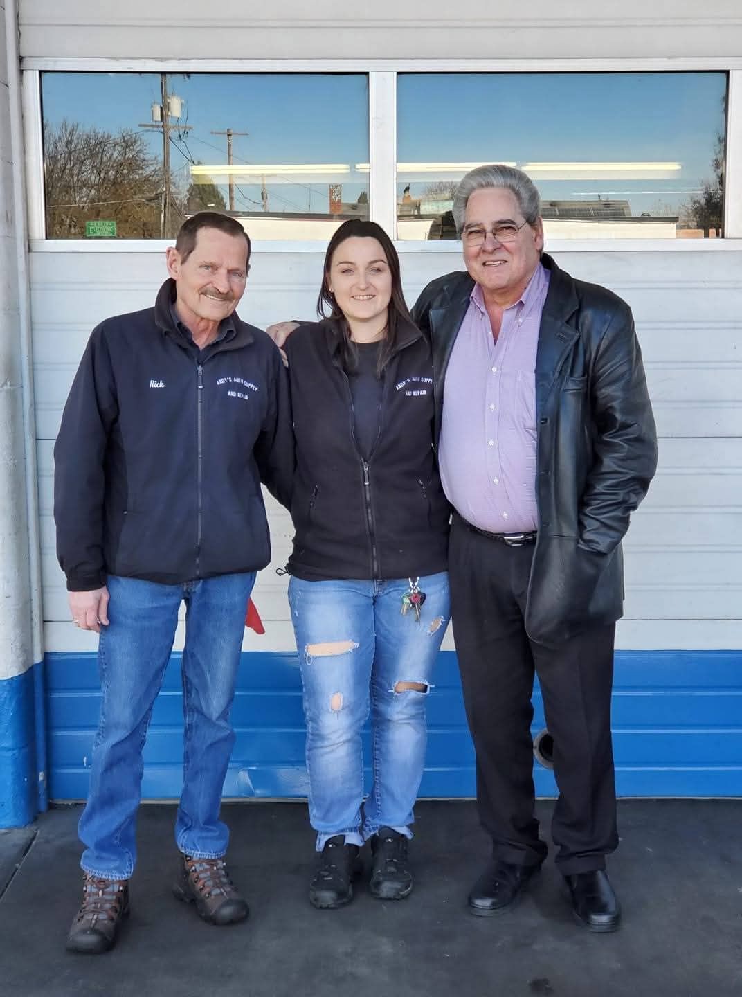 Three people stand smiling in front of a white garage door with blue trim.