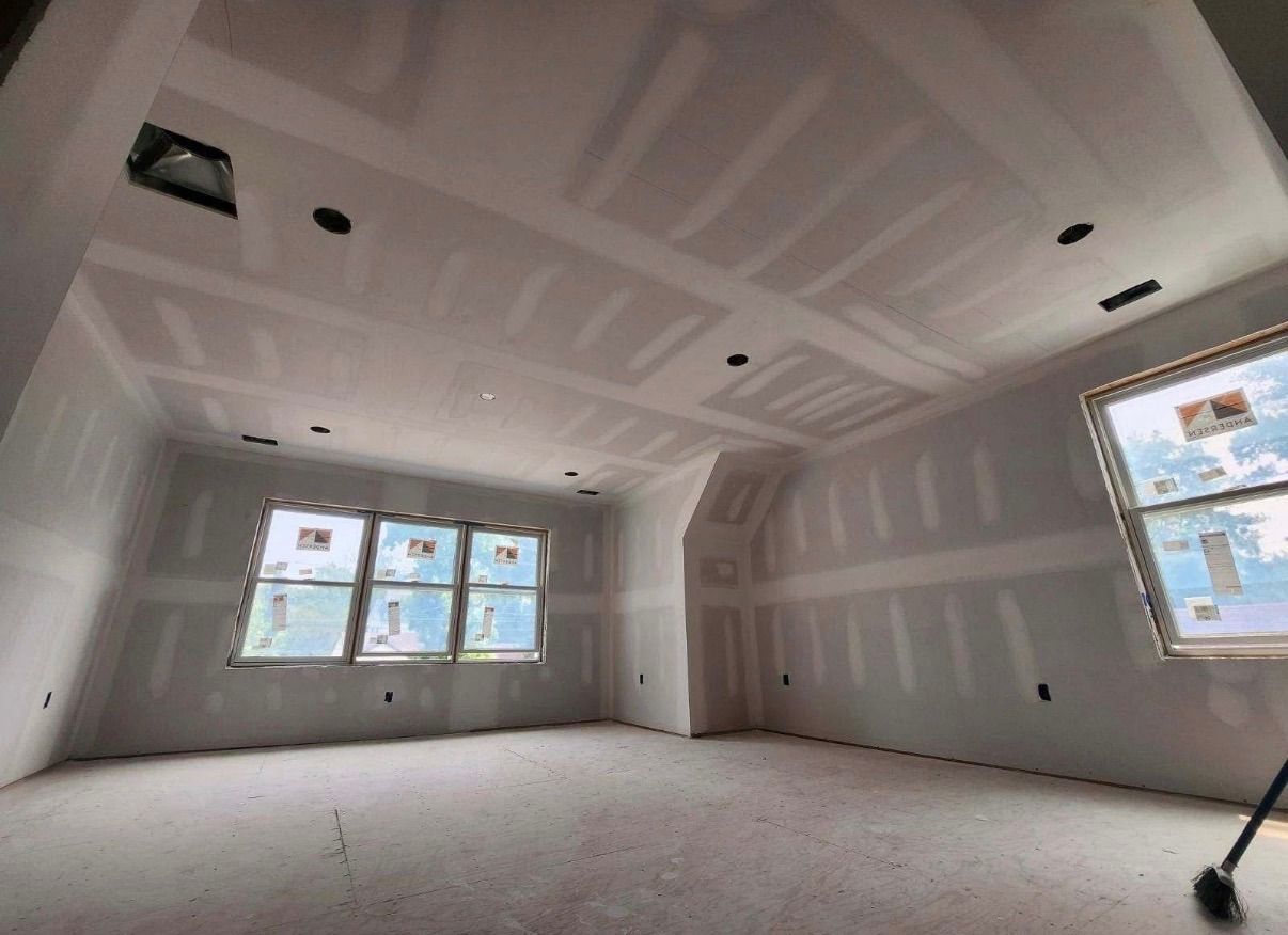 Empty unfinished room with drywall, recessed lights, and large windows letting in daylight