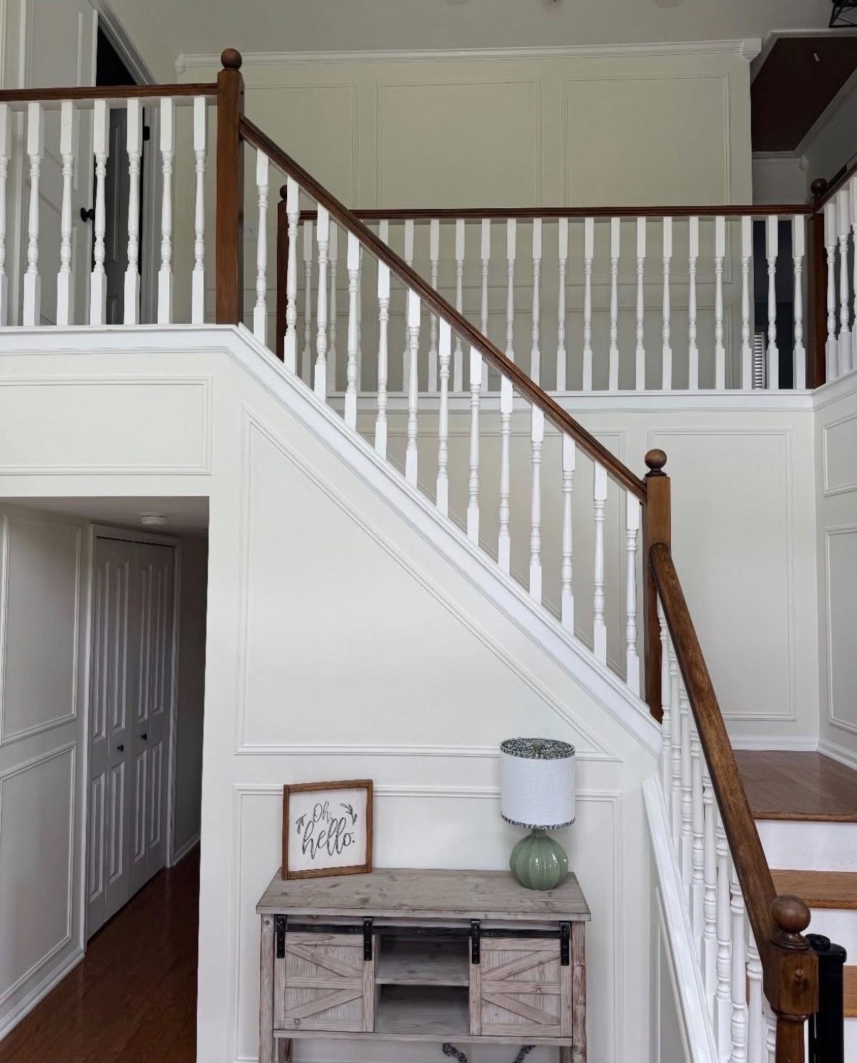 Interior staircase with white banisters, wood handrail, and small table beneath it.