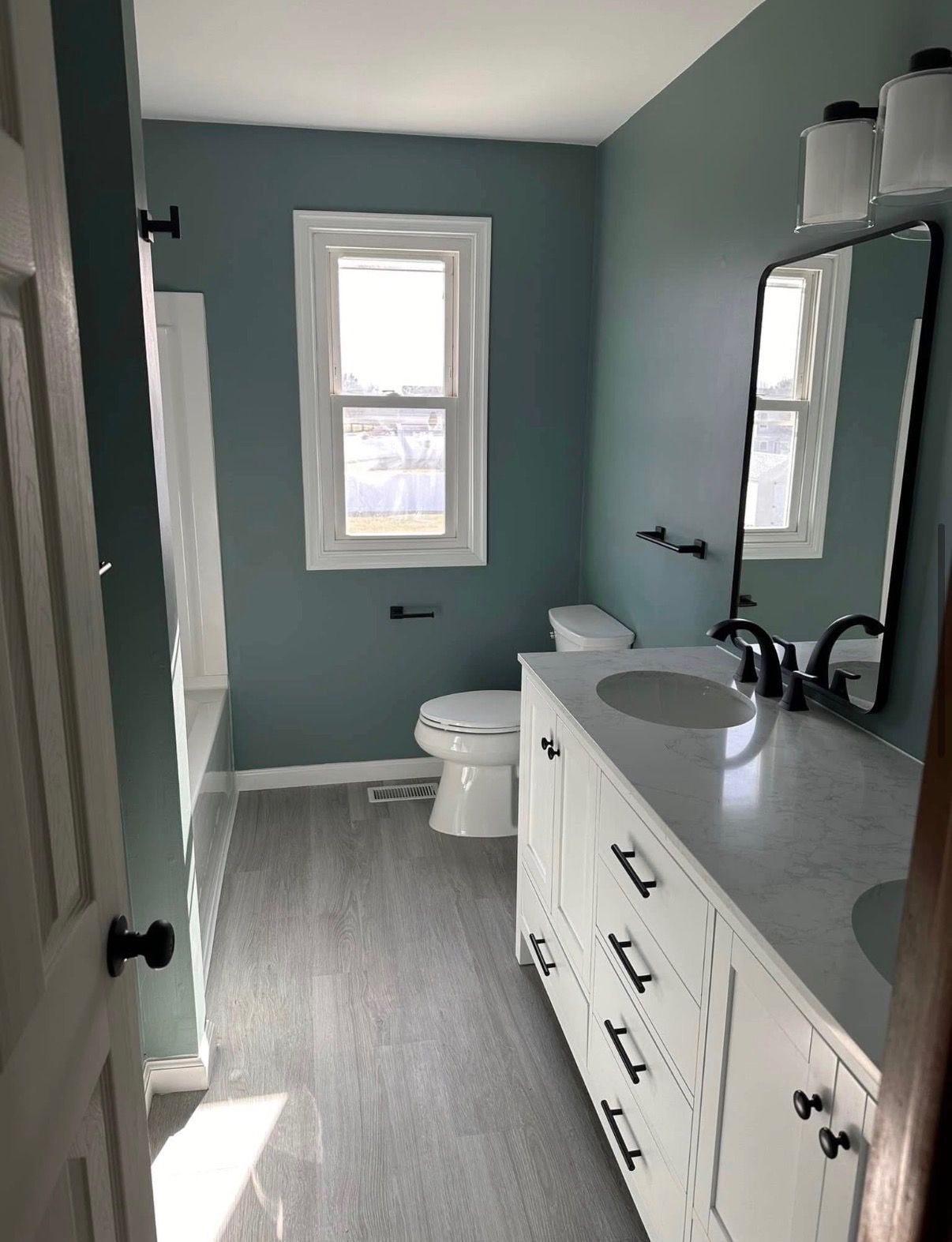 Bright bathroom with teal walls, white vanity, mirror, toilet, and window.