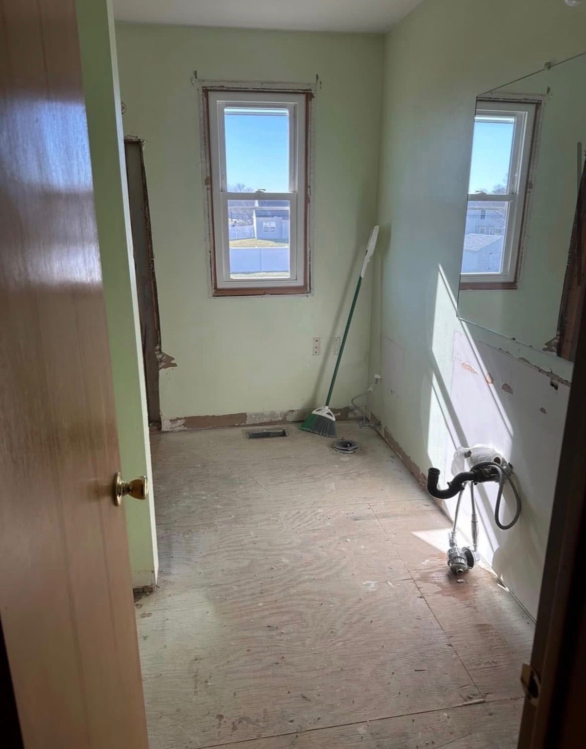 Under development bathroom with green walls, two windows, and a broom leaning near the far wall.