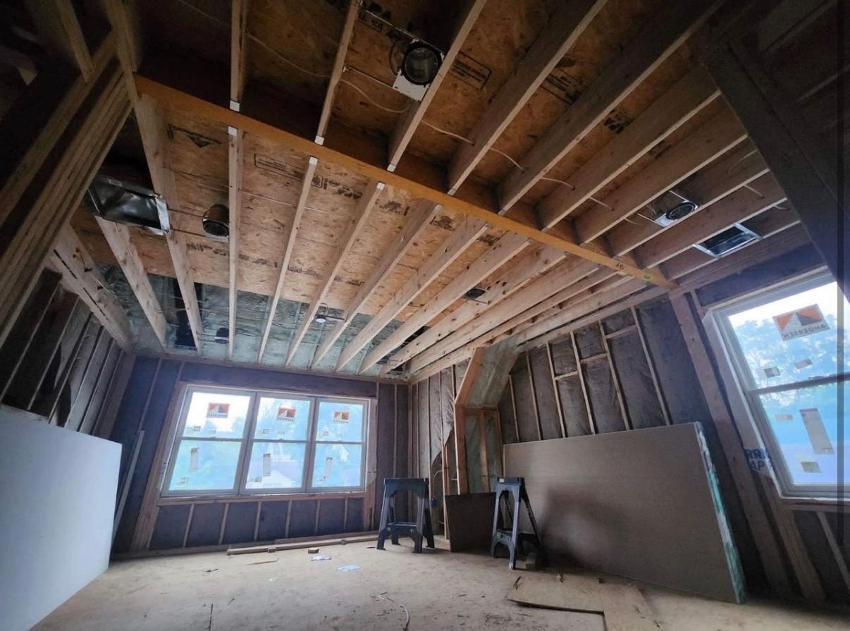 Unfinished room with exposed ceiling joists, drywall, and large windows letting in daylight.