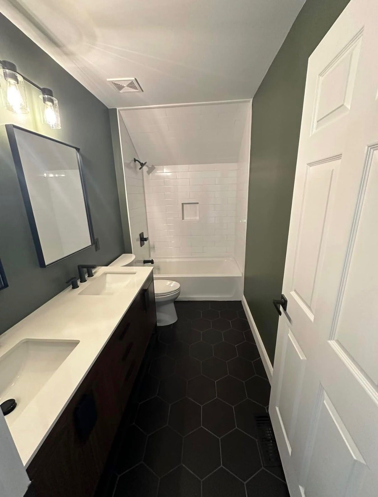 Small modern bathroom with a double sink vanity, mirror, toilet, and white-tiled shower.