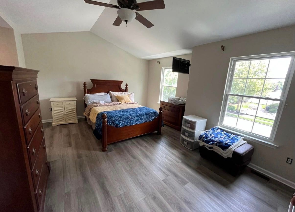 Bright bedroom with wood bed, dresser, crib, and large window on a hardwood floor
