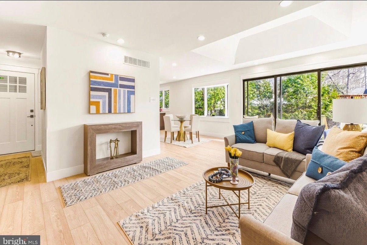 Bright living room with gray sofa, yellow cushions, fireplace, and large windows overlooking greenery