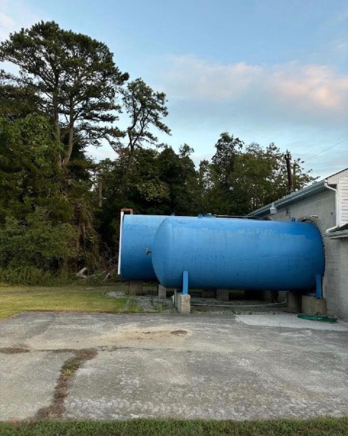 Large blue cylindrical tank beside a building on a concrete pad, with trees in the background.